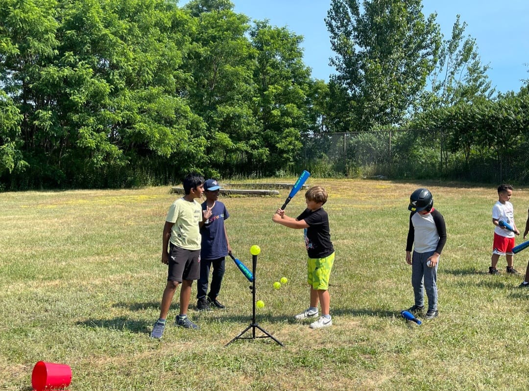 Youth baseball teammates gathered around batting tee